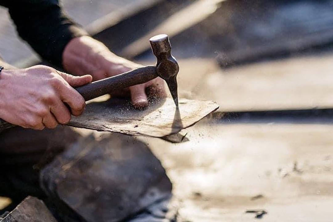 Hur lägger man skiffertak? Bilden föreställer en skifferspecialist som gör nya spikhål i en skifferplatta med hjälp av en pikhammare.